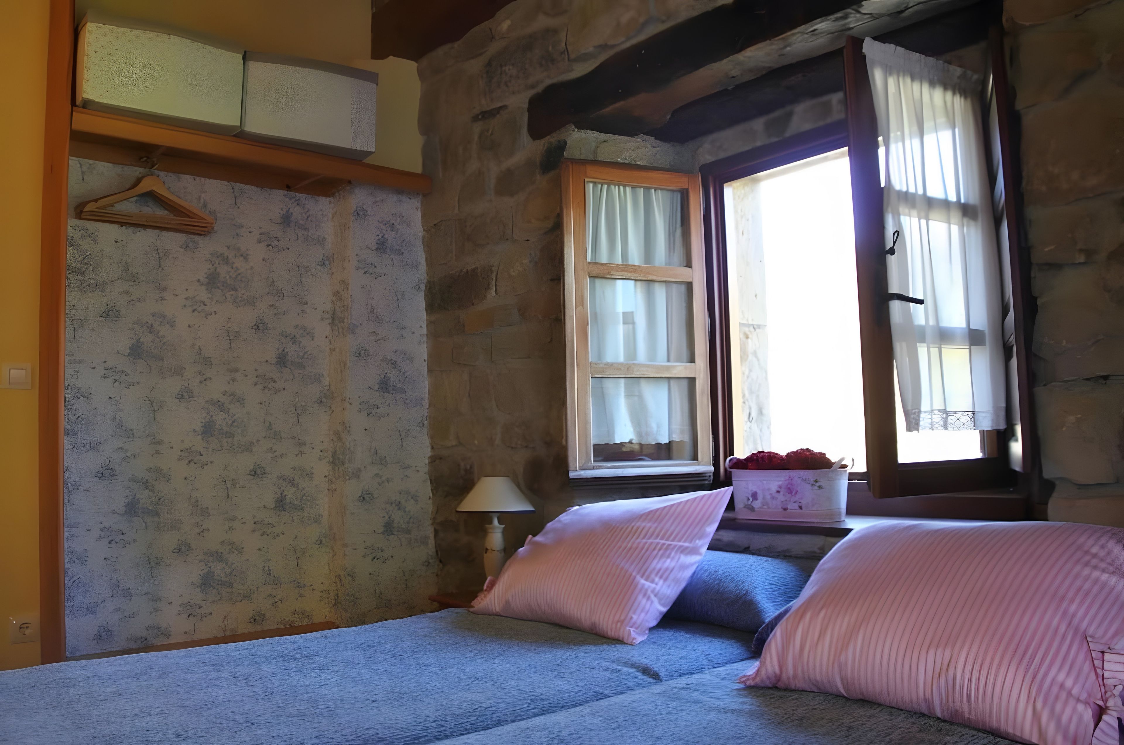 A room with a bed, a window with curtains, a lamp, and a wall with a textured pattern.