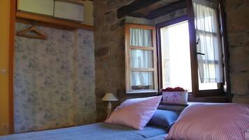 A room with a bed, a window with curtains, a lamp, and a wall with a textured pattern.