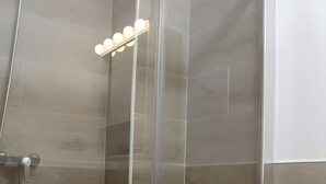 Eine Duschkabine mit Glaswänden, einer Handbrause und einer Wandleuchte.