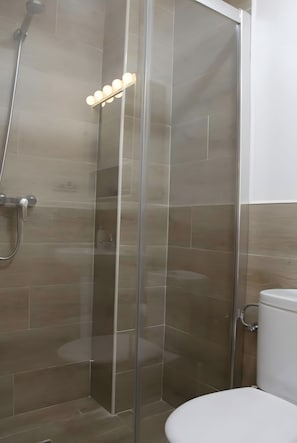 Un box de ducha con paredes de vidrio, un cabezal de ducha de mano y un aplique en la pared.