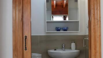 A bathroom with a pedestal sink, a mirror with lights, a toilet, and a wooden door.