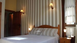 Ein Hotelzimmer mit einem Bett, zwei Nachttischlampen, einem Nachttisch, einem hölzernen Kopfteil und einem Fenster mit Vorhängen.