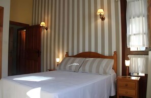 Habitación de hotel con cama, dos lámparas de noche, una mesita de noche, un cabecero de madera y una ventana con cortinas.
