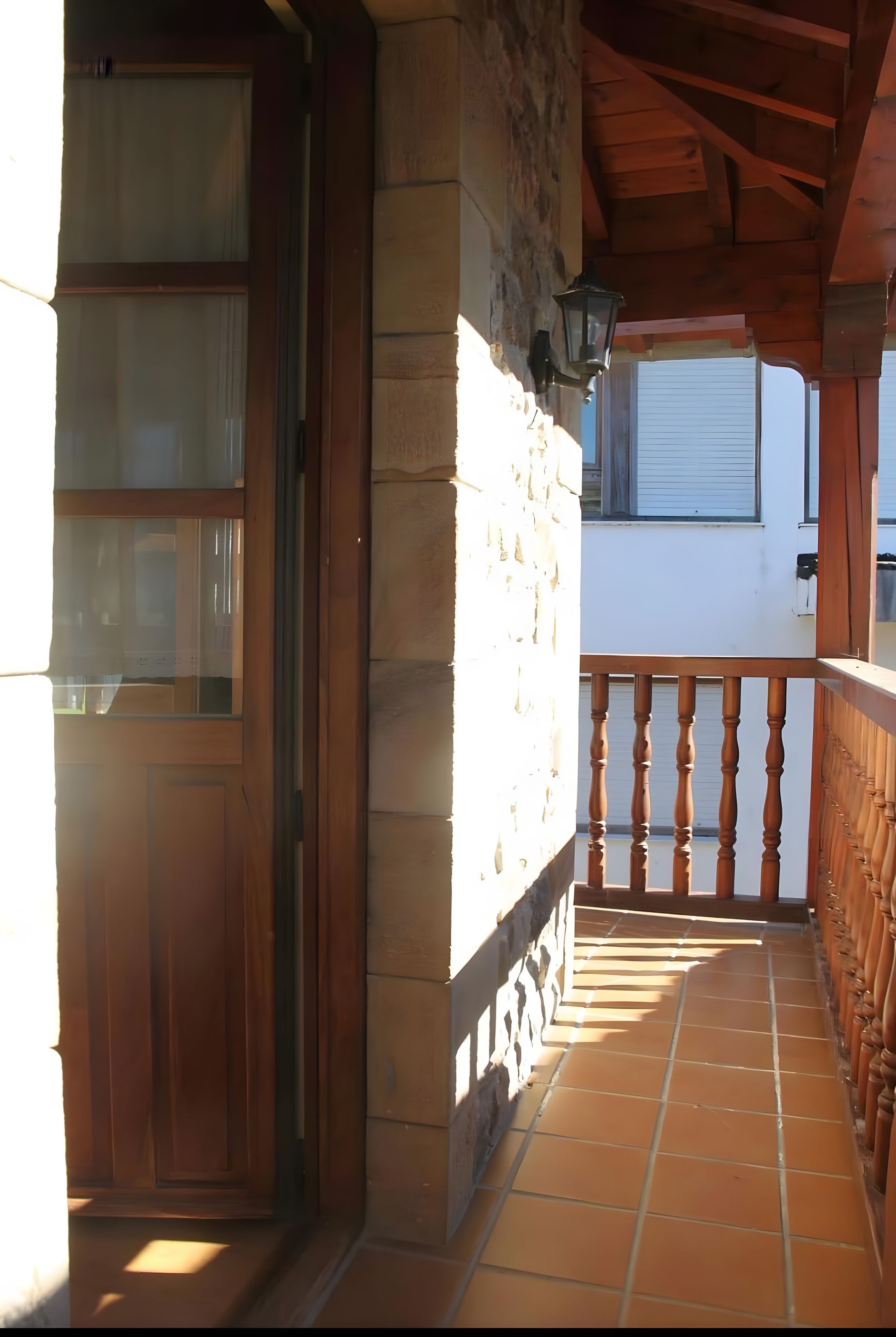 Un balcón de madera con un muro de piedra, una puerta de madera y una ventana.