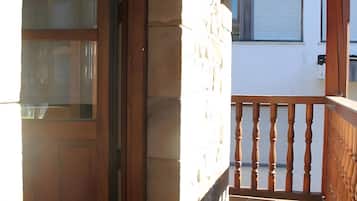 Un balcón de madera con un muro de piedra, una puerta de madera y una ventana.