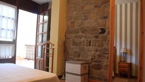 Ein Zimmer mit einem Bett, einem Holzstuhl, einer Steinwand und einem kleinen Tisch mit einer Lampe.