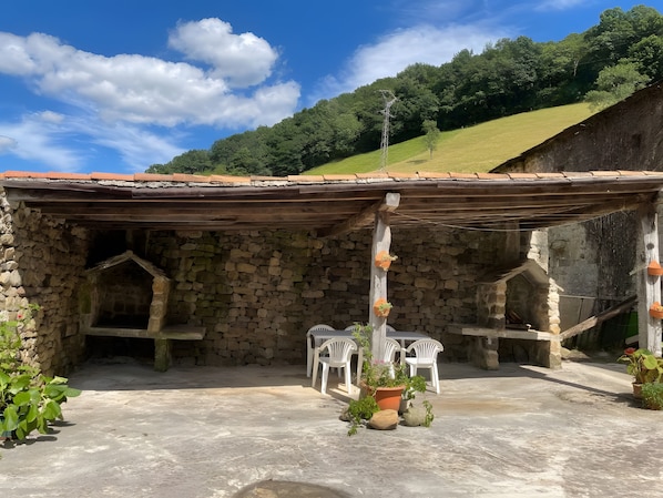 A stone building with a tiled roof, outdoor seating area, and potted plants.