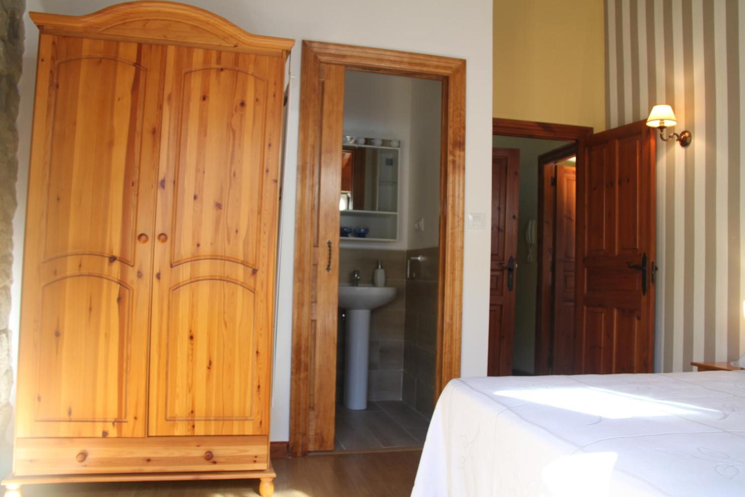 Una habitación con armario de madera, baño con lavamanos y cama con cubrecama blanco.