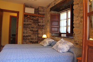 Un dormitorio con pared de piedra, una cama con ropa de cama estampada y una ventana con contraventanas de madera.