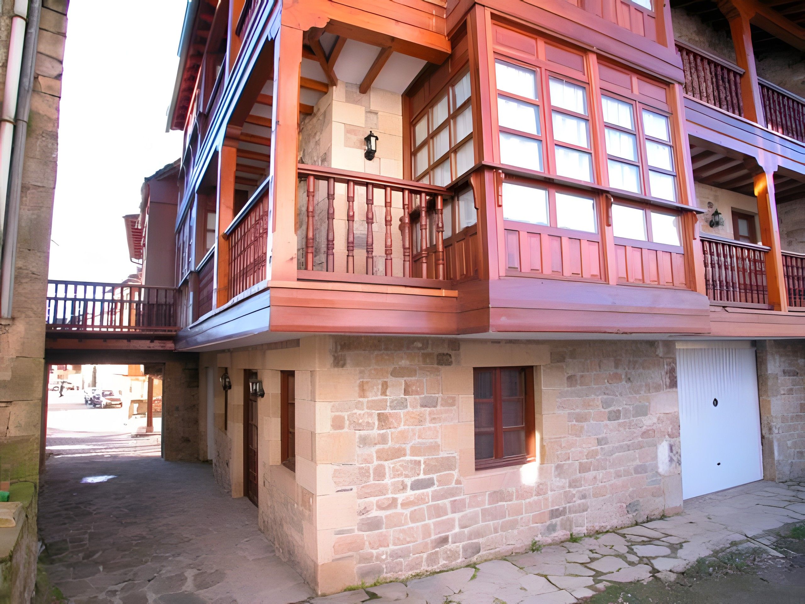 Un edificio de varios pisos con fachada de piedra, balcones con barandillas de madera y una puerta de garaje visible.