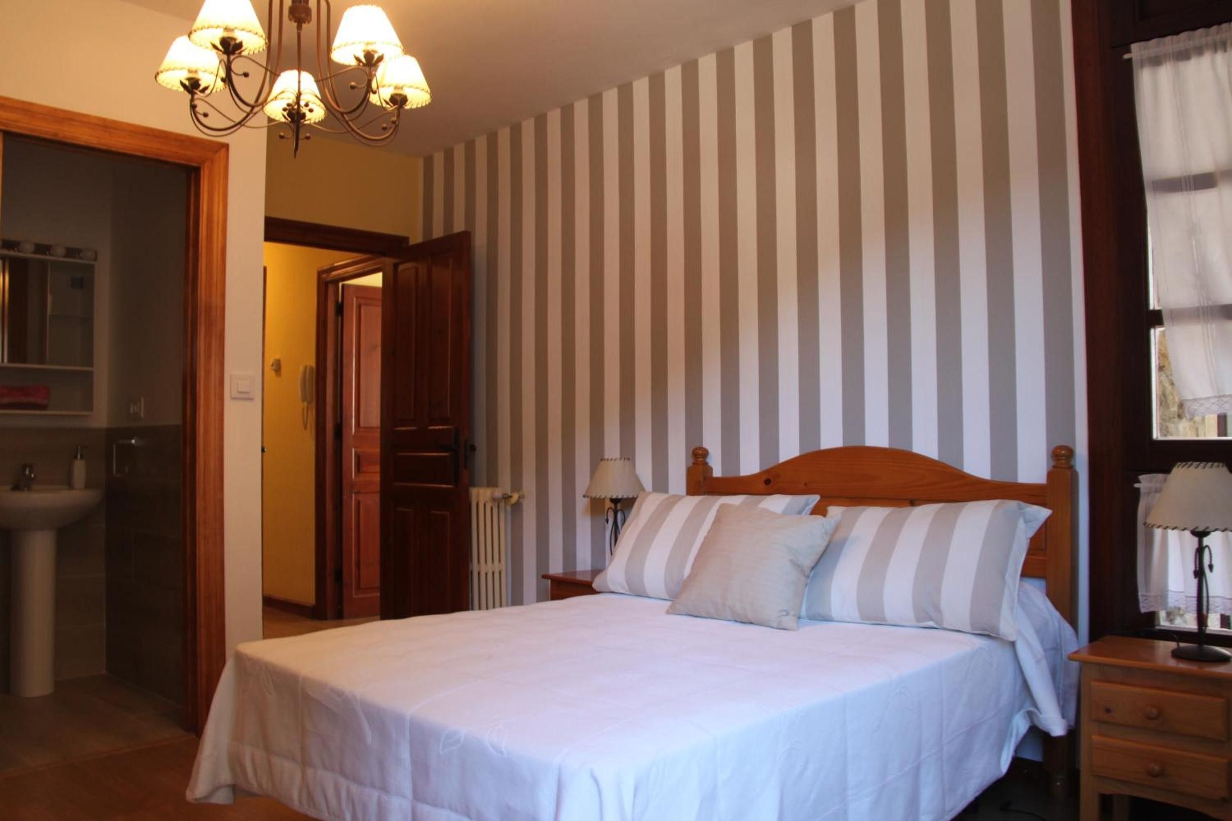 Un dormitorio con cama, mesita de noche, lámpara, cómoda y baño con lavabo y espejo.