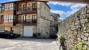 Ein Steinhaus mit einem hölzernen Balkon, einem parkenden Auto und einem Fahrrad mit Korb.
