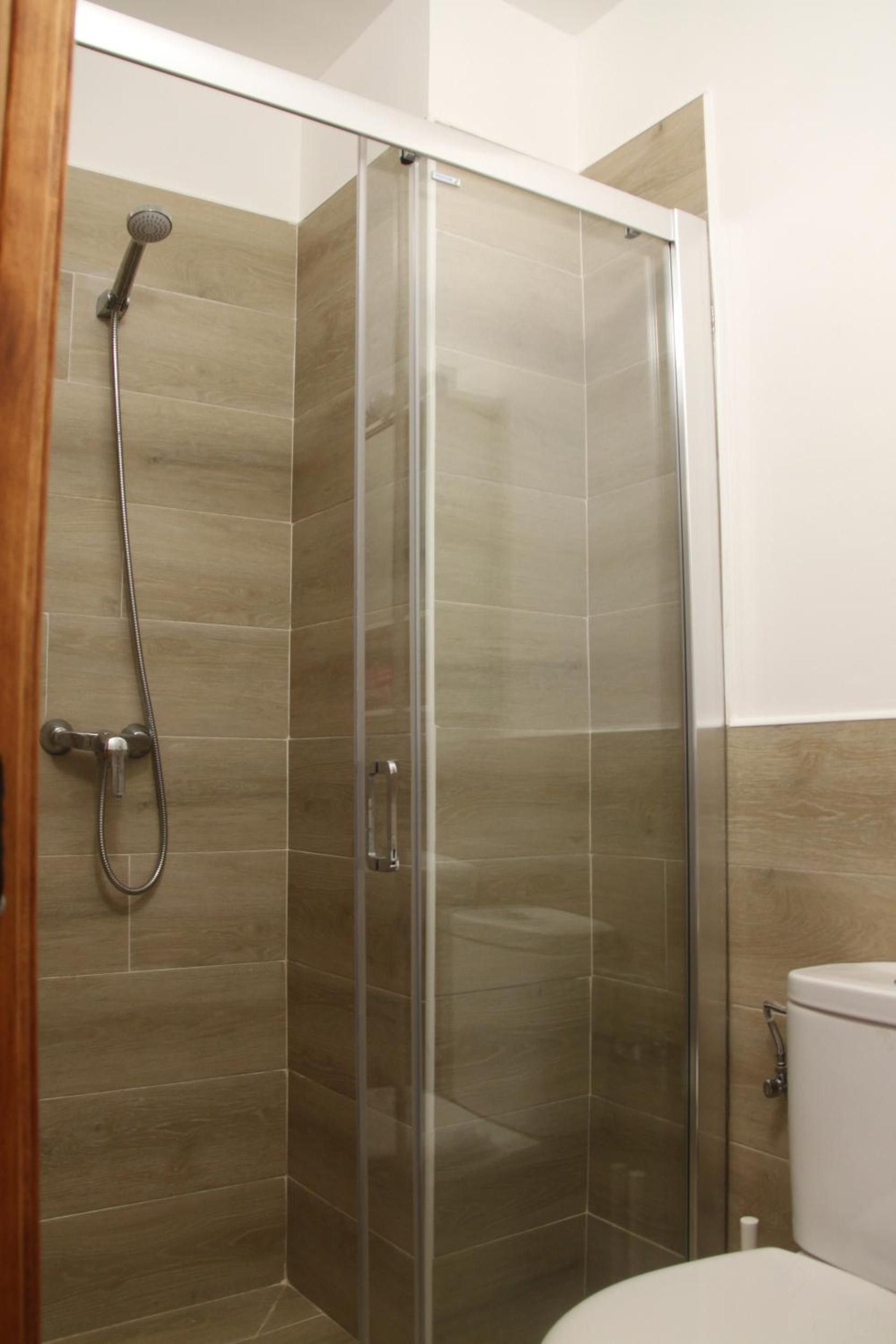 Cabina de ducha con puerta de vidrio, cabezal de ducha manual y un inodoro a la derecha.