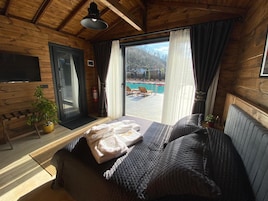 Habitación de cabaña de madera con cama, una planta en maceta, extintor y vistas a una piscina y zona de estar exterior.