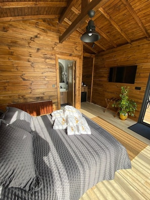 A wooden cabin room with a bed, a television, and a potted plant. - King Tiny House (Karamandere)