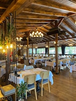 Restaurante com vigas de madeira, lustres e mesas preparadas para refeições.