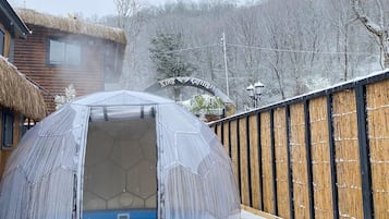 Eine geodätische Kuppel mit offenem Eingang, umgeben von einer Holzterrasse und verschneiter Erde.