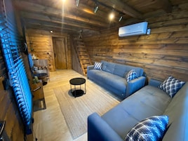 Interior acogedor de una cabaña de troncos con un sofá azul, una pequeña mesa redonda y una escalera que lleva a una zona de altillo.