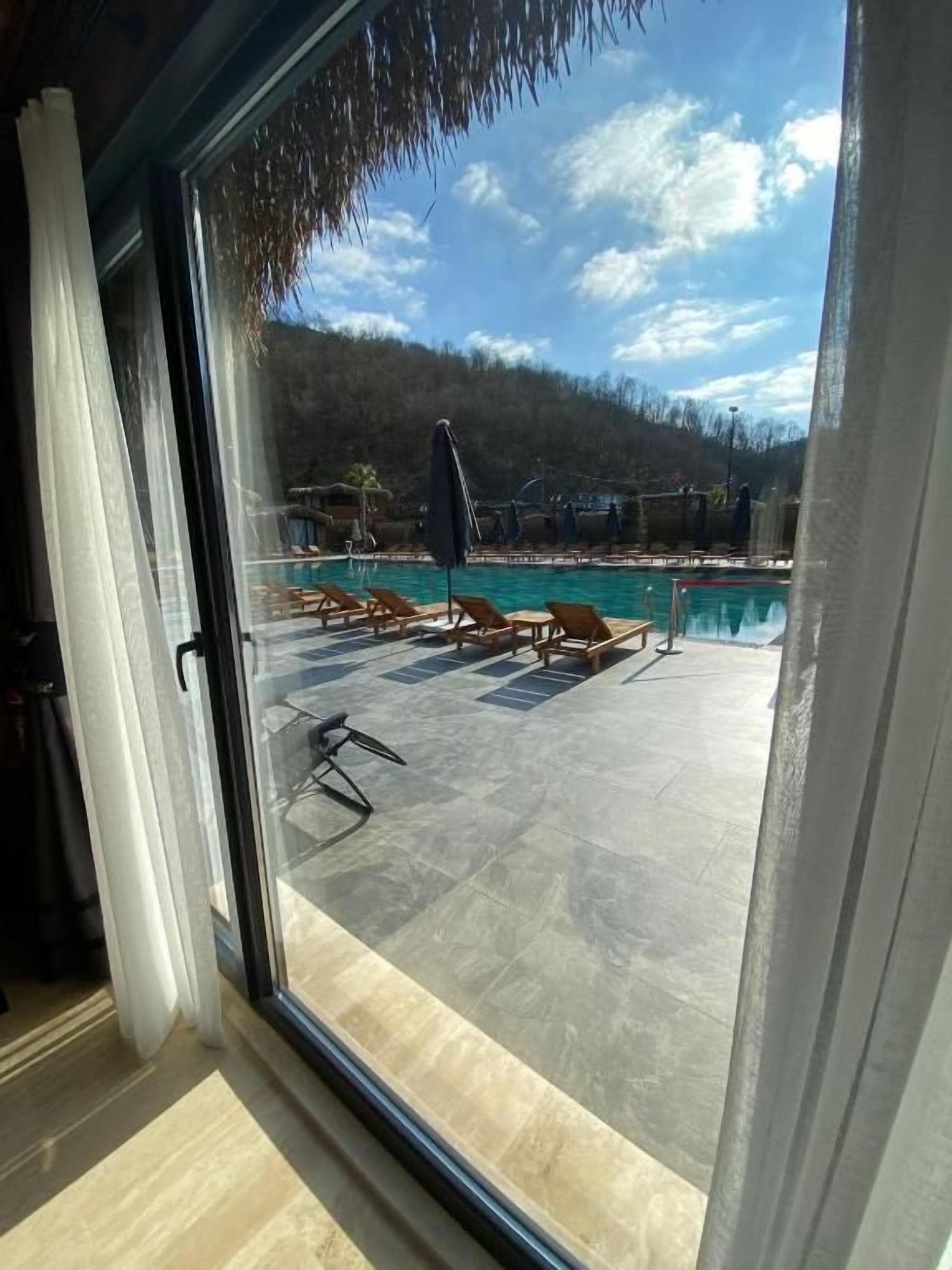 Vista pela janela de uma área de piscina com espreguiçadeiras e guarda-sóis.