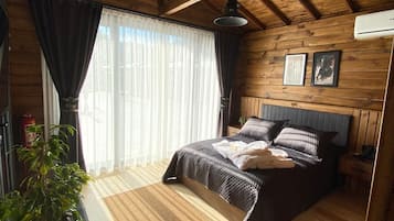 Ein Schlafzimmer mit Holzboden, einem Bett mit dunklem Kopfteil, einem Nachttisch, einer Topfpflanze und einem Fenster mit Vorhängen.