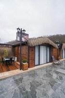 Uma cabana de madeira com telhado de palha, uma sala de jantar com mesa e cadeiras, e um pequeno jardim.