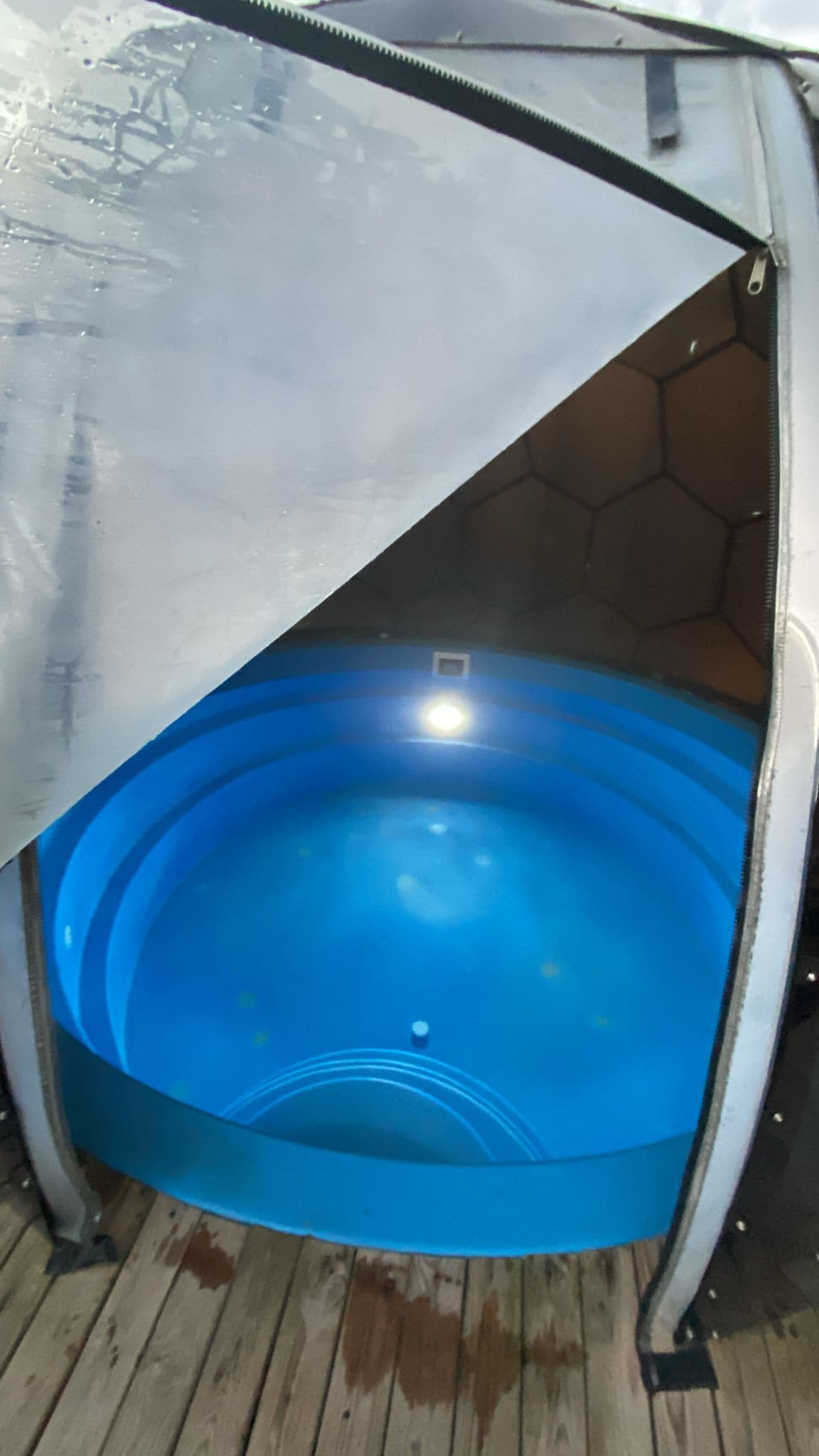 A hot tub with a transparent cover, surrounded by a hexagonal structure.