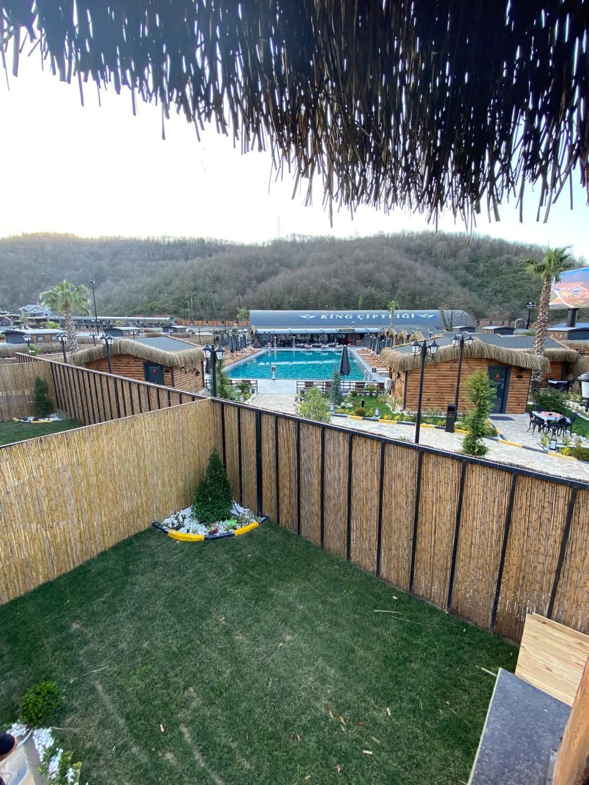 A pool area with a wooden fence, a small tree, and a building with a sign.
