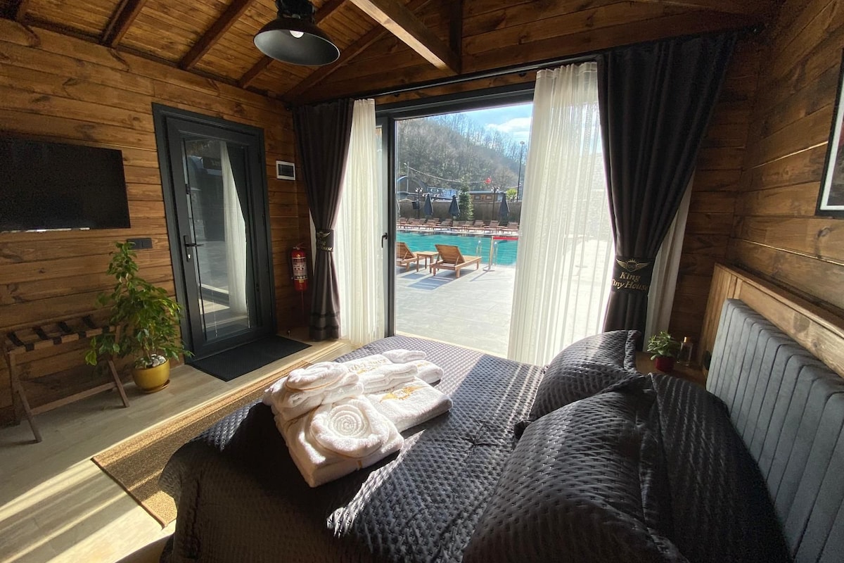 A room with a bed, a potted plant, a fire extinguisher, and a view of an outdoor swimming area.
