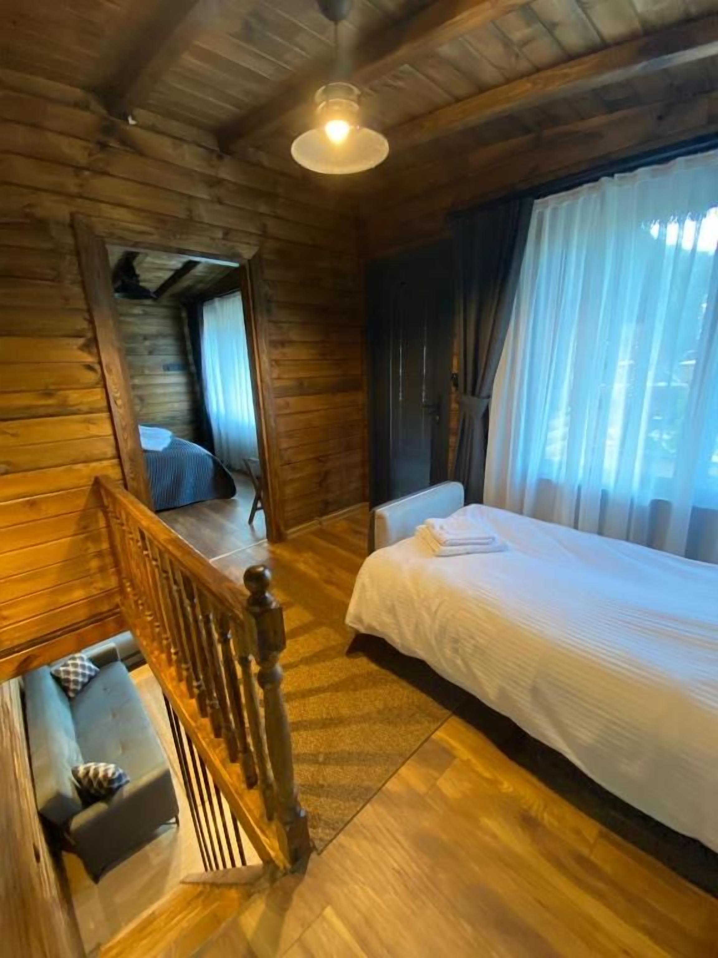 Un dormitorio tipo cabaña de madera con cama, una ventana con cortinas, una escalera y un pequeño rincón de descanso.