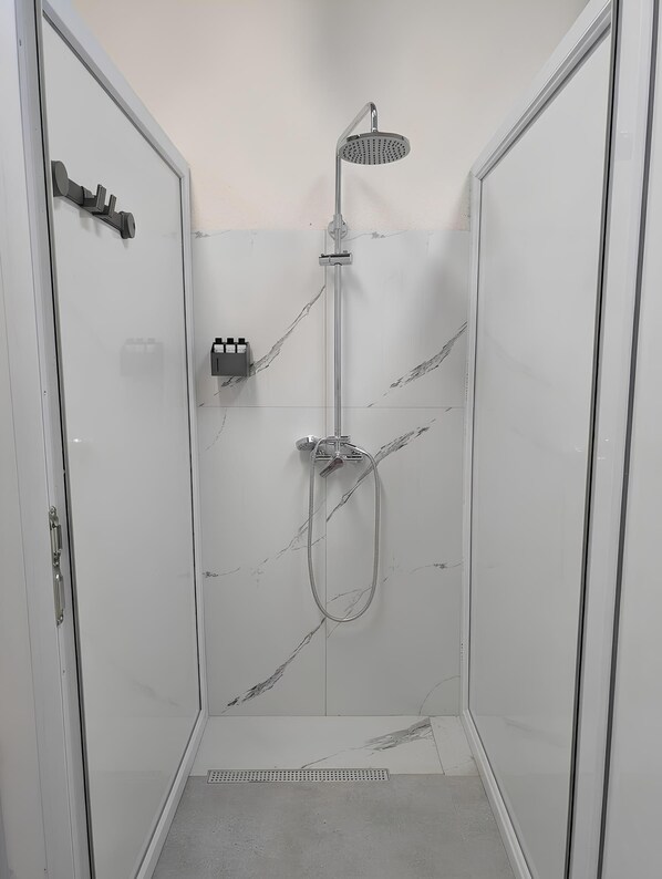A walk-in shower with a handheld showerhead, a wall-mounted control panel, and a floor drain.