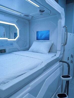 Una habitación futurista con una cama, un panel de control, un monitor y un pequeño taburete.