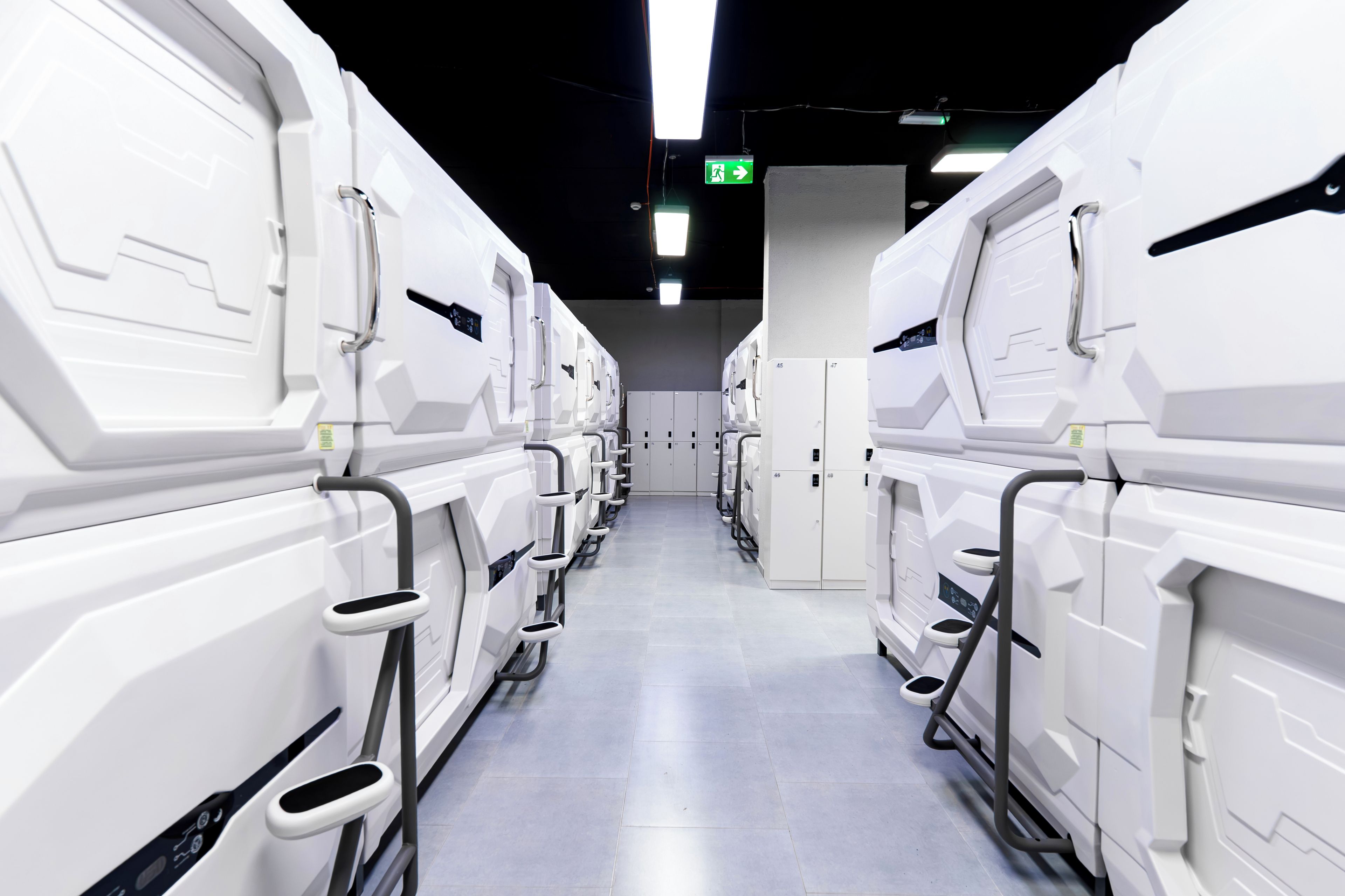 A row of white, modern-looking, rectangular units with handles, possibly a row of portable toilets or similar facilities, in a clean, well-lit corridor.