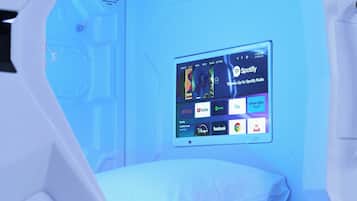 Een kamer met een bed, een aan de muur bevestigde televisie waarop verschillende streamingdiensten worden weergegeven, en een ventilatiesysteem.