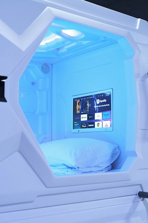 Una habitación con cama, televisor de pared que muestra diversos servicios de transmisión y sistema de ventilación.