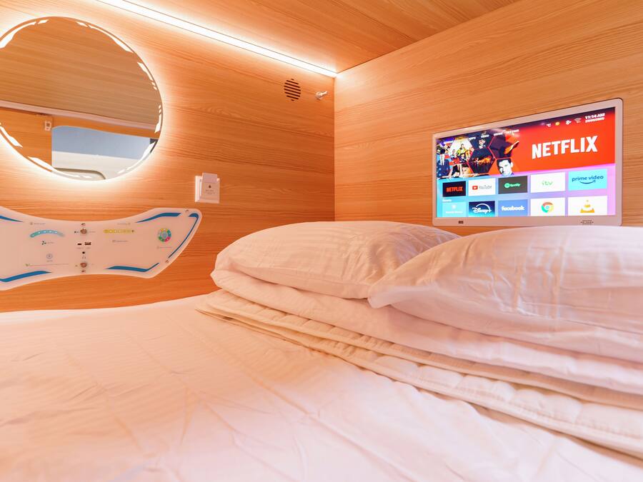 Habitación de hotel con cama, mesita de noche, televisor de pared mostrando la interfaz de Netflix y un espejo circular sobre la cama.