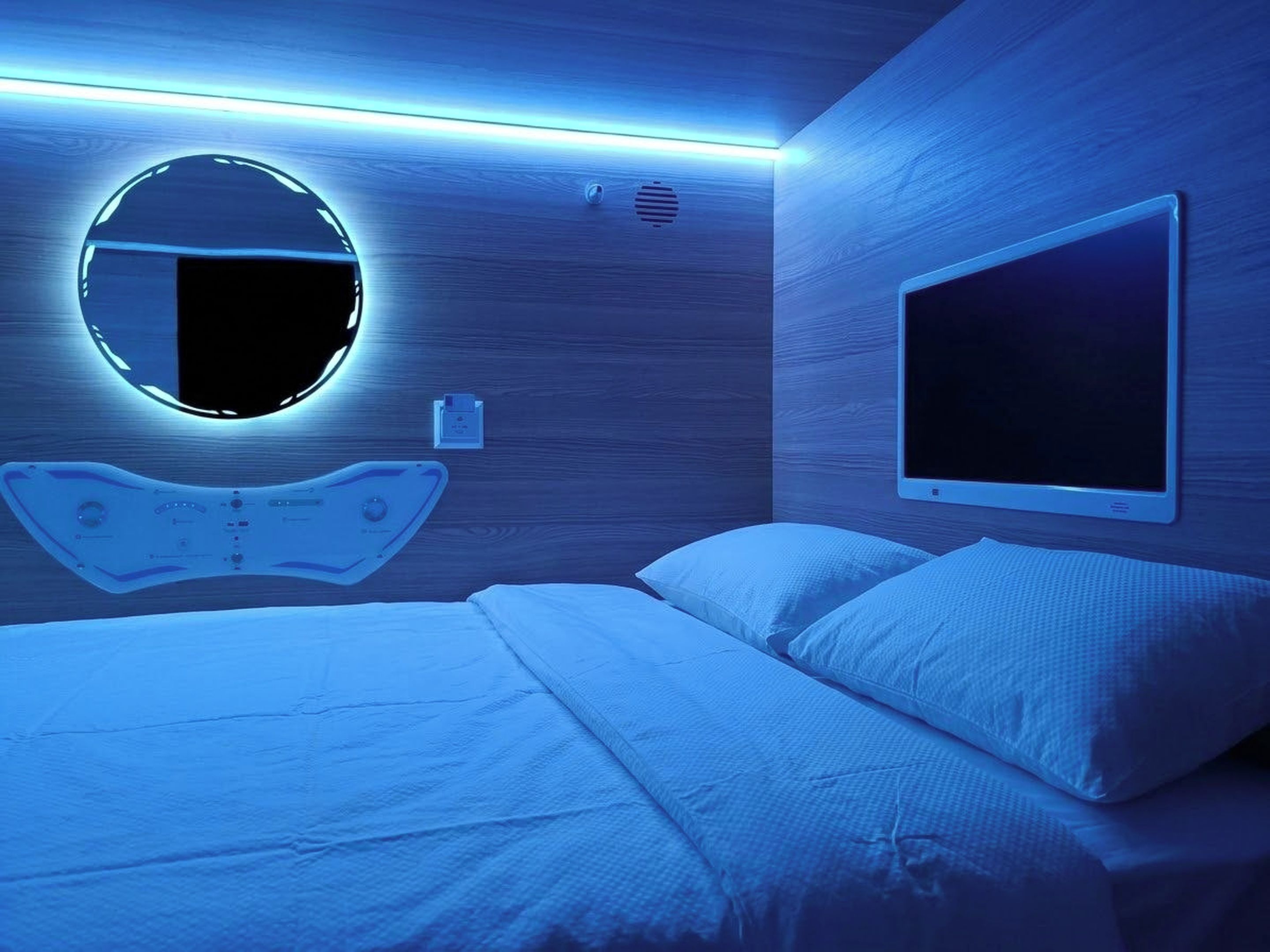Een moderne slaapkamer met een bed, een ronde spiegel en een tv aan de muur.