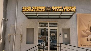 L'entrée de l'hôtel-capsule Happy Lounge est clairement indiquée par un panneau, un escalier y mène, et un petit jardin se trouve devant.
