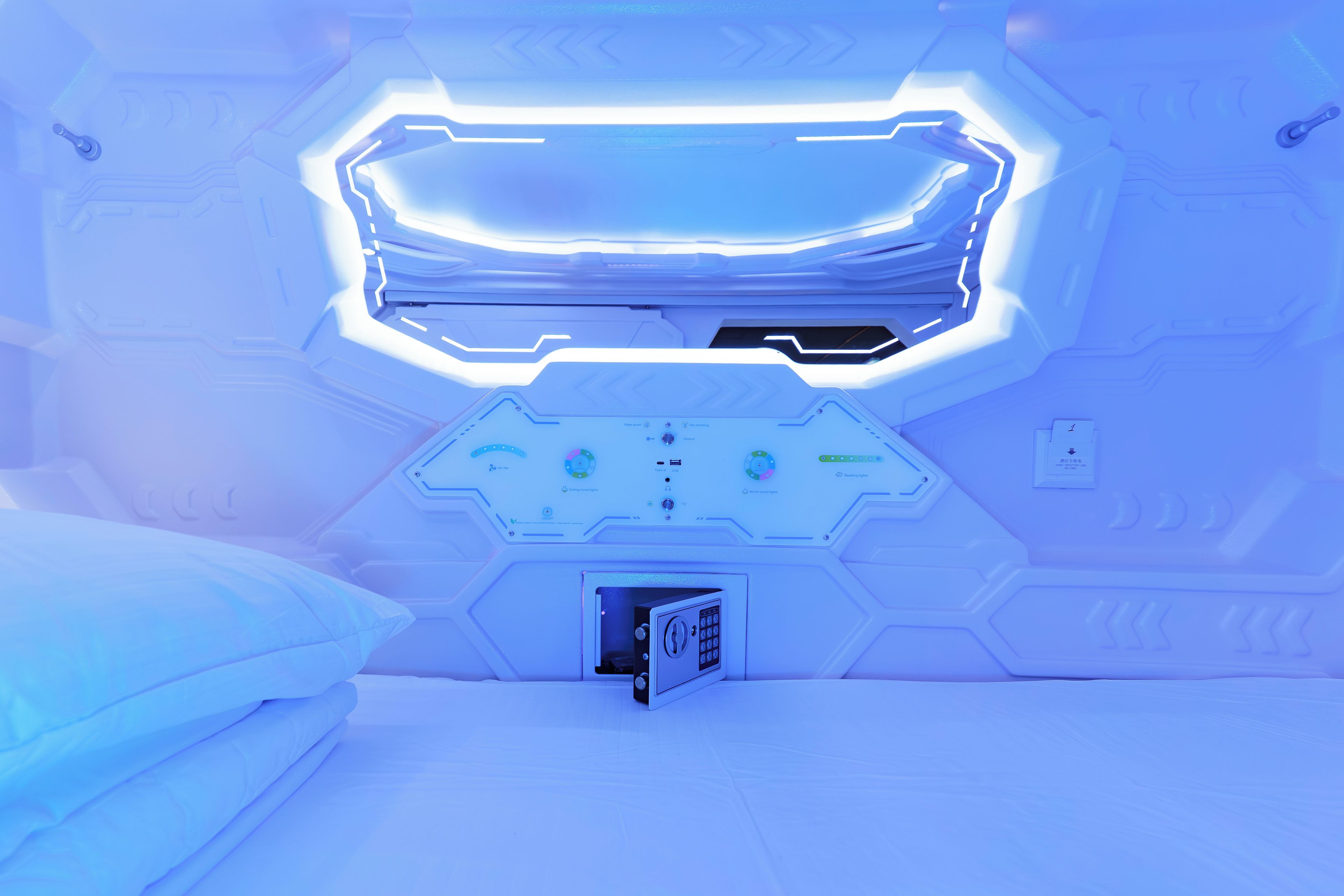 A futuristic room with a central control panel, a bed, and a small device on the floor.