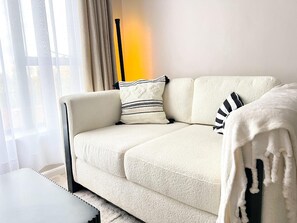 A white sofa with a textured cover, a striped pillow, and a black and white striped pillow. There is a white throw blanket draped over the sofa. - Marvelous 1-bedroom apartment in the heart of Kiambu road (Kiambu)