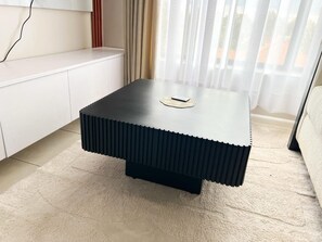 A modern, square coffee table with a ribbed design, placed on a textured rug in a room with a white cabinet and sheer curtains. - Marvelous 1-bedroom apartment in the heart of Kiambu road (Kiambu)