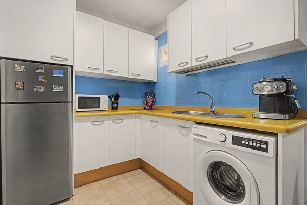 A compact kitchen with a stainless steel refrigerator, a microwave, a coffee maker, and a washing machine.