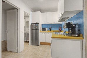 A compact kitchen with white cabinets, a stainless steel refrigerator, a microwave, and a coffee machine.
