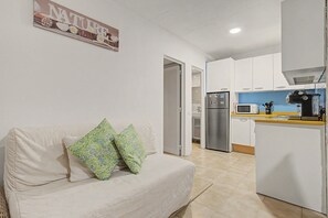 A compact living space with a kitchenette, a sofa with patterned cushions, and a wall-mounted sign.