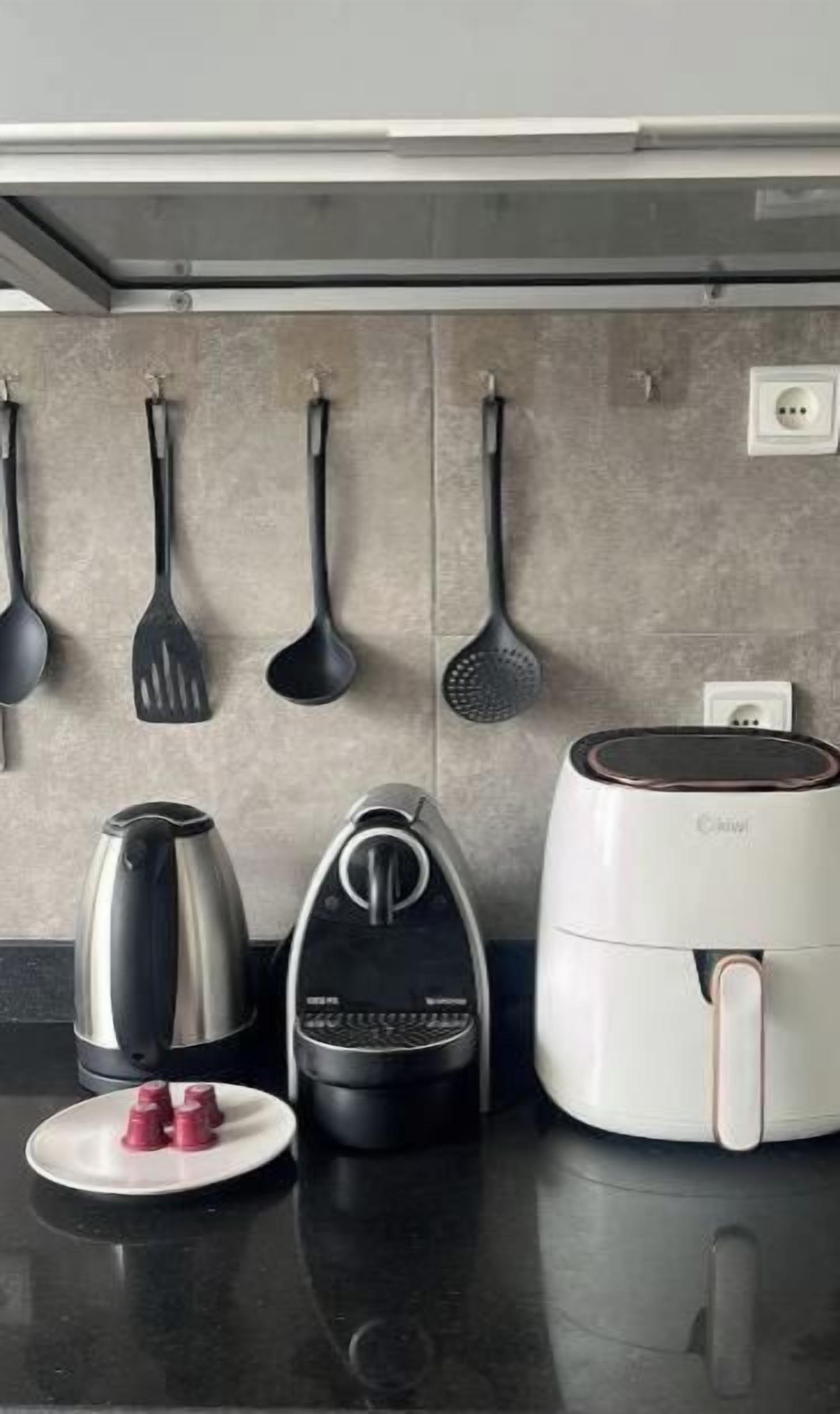 Un plan de travail de cuisine avec une bouilloire, une machine à café, un cuiseur à riz et un ensemble d’ustensiles de cuisine.