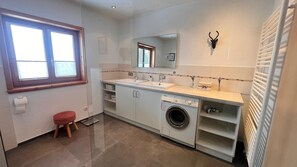 Ein modernes Badezimmer mit Waschmaschine, Waschbecken, Spiegel und einem roten Hocker.