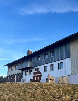 Ein zweistöckiges Gebäude mit einem Schild, das 'Apfel Stadt 11' zeigt, und einem Balkon im oberen Geschoss.
