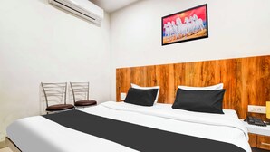 A hotel room with a bed, two chairs, a wooden headboard, a painting, and an air conditioning unit. - Collection O Indore Gandhi Hall (Indore)