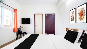 A hotel room with two beds, a TV mounted on the wall, a window with curtains, and artwork on the wall. - Collection Rushikonda Beach Near GITAM (Visakhapatnam)