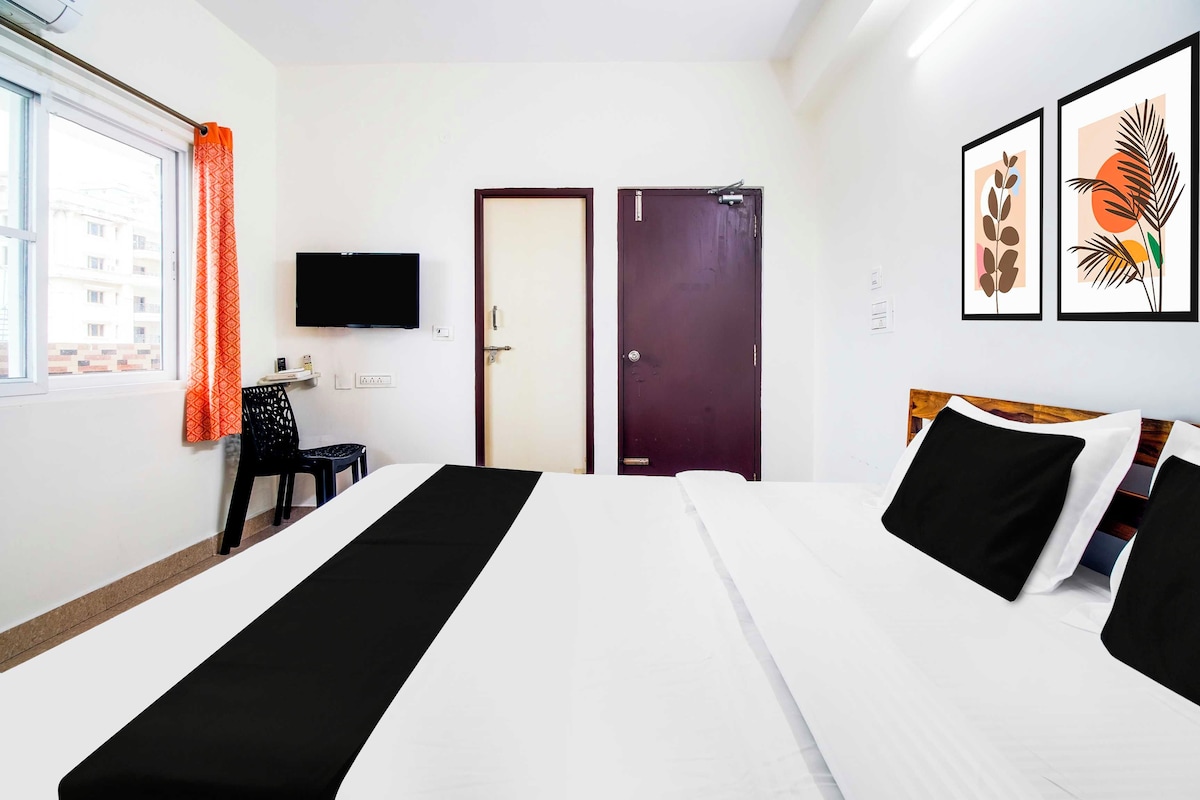 A hotel room with two beds, a TV mounted on the wall, a window with curtains, and artwork on the wall.