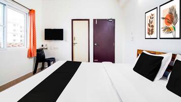 A hotel room with two beds, a TV mounted on the wall, a window with curtains, and artwork on the wall.